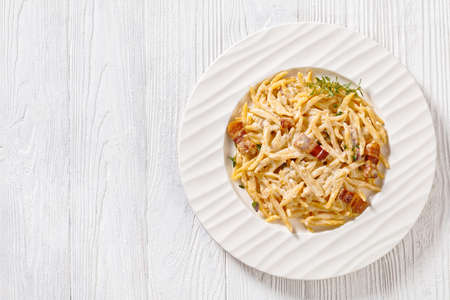 delicious capunti pasta in cream pecorino cheese and pancetta sauce on white plate on white wooden table, italian cuisine, horizontal view above, flat lay, free spaceの写真素材