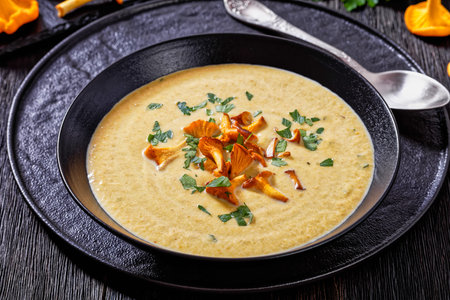 Kanttarellikeitto, Finnish Chanterelle Soup in black bowl on dark wooden table with spoon, horizontal view from above, close-upの写真素材