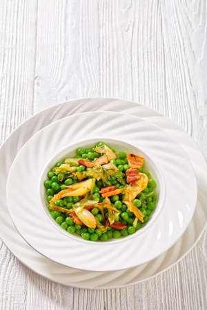 petits pois, french dish of tender, new-season peas braised in chicken stock with lettuce, onion bulbs and speck, cut into lardons, served in white bowl, vertical view, free spaceの写真素材
