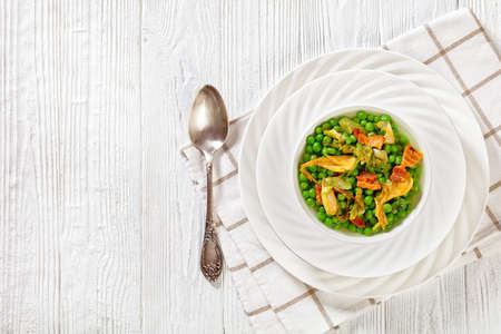 petits pois, french dish of tender, new-season peas braised in chicken stock with lettuce, onion bulbs and speck, cut into lardons, served in white bowl, flat lay, free spaceの写真素材