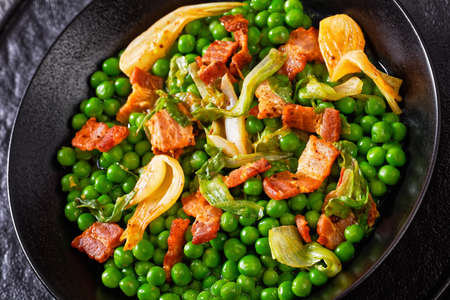 petits pois, french dish of tender, new-season peas braised in chicken stock with lettuce, onion bulbs and speck, cut into lardons, served in black bowl, close-upの写真素材