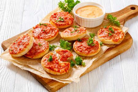 mini pizzas with ham and pecorino cheese on wooden cutting board with thousand islands sauce on white wooden table, picnic appetizer, horizontal view from above, close-upの写真素材