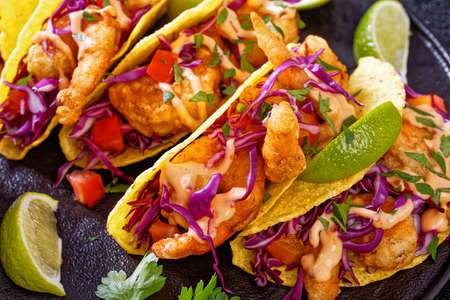 close-up of Bang Bang Shrimp Tacos with purple cabbage, tomatoes, parsley, lime drizzled with mayonnaise hot chili sauce on black plate on concrete table, horizontal view from aboveの写真素材