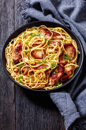Fried Chicken breast pieces with gluten free spaghetti in frying pan on dark wooden table with kitchen towel, vertical view from aboveの写真素材