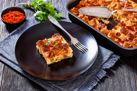portion of Scalloped Chicken Casserole topped with croutons on black plate on dark wooden table,...