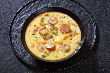 Kartoffelsuppe, German potato soup with sausages in black bowl on dark table, horizontal view from aboveの写真素材