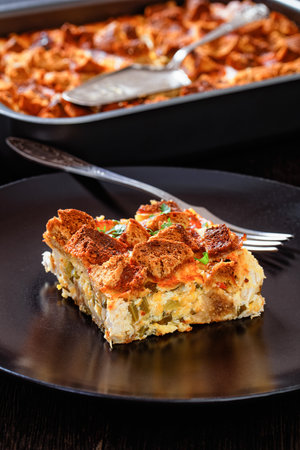close-up of Scalloped Chicken Casserole in baking dish on dark wooden table and portion on black plate, vertical view from aboveの写真素材