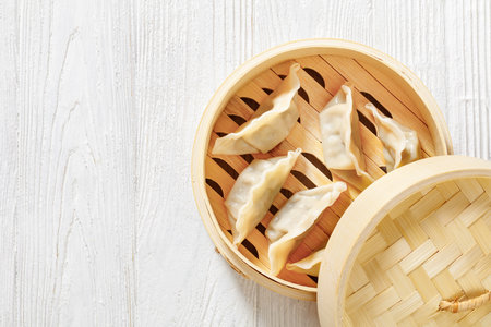 gyoza, wonton wrappers stuffed with pork and cabbage in bamboo steamer on white wooden table, horizontal view from above, flat lay, free space, close-upの写真素材