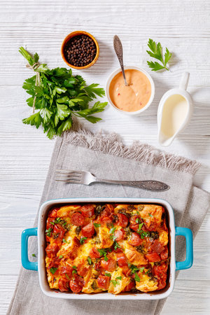 english muffin sausage breakfast casserole in baking dish on white wooden table with ingredients, vertical view from aboveの写真素材