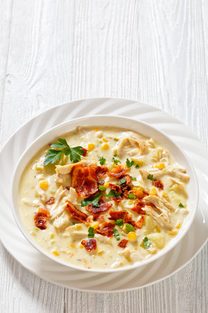 Chicken Corn Chowder, rich and creamy soup with leftover chicken breast, potatoes, sweet corn, topped with fried crispy bacon and fresh parsley in white bowl, vertical view, free spaceの写真素材