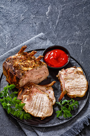 Standing Pork Rib Roast cut on chops on black plate with tomato sauce and parsley, vertical view from aboveの写真素材