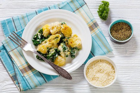 cheesy baked shell pasta with green leafy kale topped with crispy breadcrumbs on plate with fork on white wood tableの写真素材