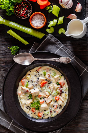 Turkey Wild Rice Soup with red potatoes. carrot, celery, spices and herbs in black bowl on dark wooden table with ingredients, vertical view from aboveの写真素材