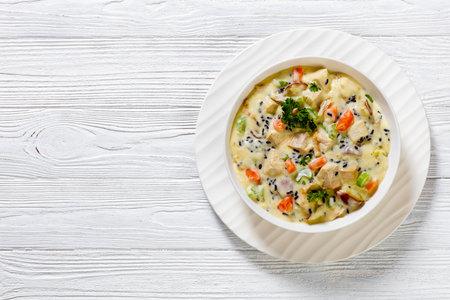 Turkey Wild Rice Creamy Soup with red potatoes. carrot, celery, spices and herbs in white bowl on wooden table, flat lay, free spaceの写真素材
