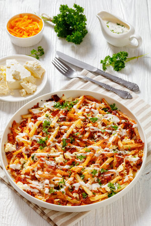 Bacon Mozzarella Feta Cheddar Cheese Fries with ranch dressing and parsley on white dish on wood...