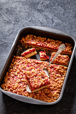 Raspberry Crumble Bars in baking dish on concrete table with cake shovel, vertical view from aboveの写真素材