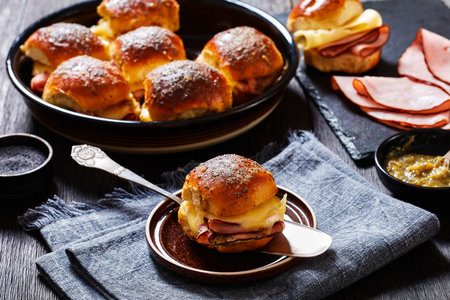 close-up of Ham and Cheese Hawaiian Roll Slider on cake shovel and iin backing dish on dark wood table, landscape view aboveの写真素材