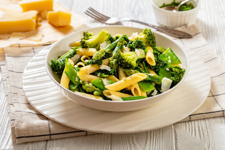 Pasta penne primavera with asparagus, snap peas, broccoli and kale in white bowl on white wood tableの写真素材
