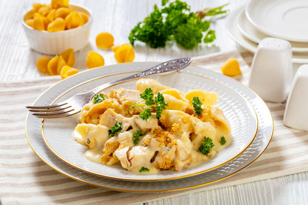 cheesy and creamy chicken and shells pasta bake in white bowl with fork on white table, horizontal view from above, close-upの写真素材