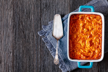 vegan Cauliflower Cheese bake in baking dish on dark wood table with cake shovel, horizontal view from above, flat lay, free spaceの写真素材