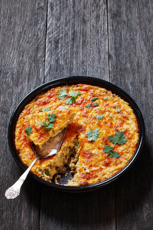 Cheesy Loaded Grits casserole with ground beef meat in baking dish on dark wood table, vertical view, free spaceの写真素材