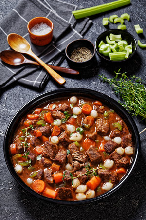 boneless beef short ribs stew with carrots and pearl onions in black bowl on concrete table with...