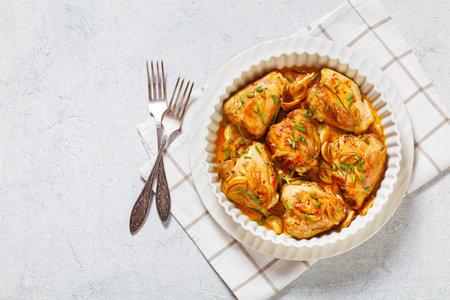 garlic rosemary thyme herbed baked chicken thighs in white baking dish on concrete table with forks, horizontal view from above, flat lay, free spaceの写真素材