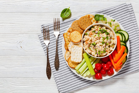 healthy easy leftover salmon salad served with fresh carrots, cucumber, celery, tomatoes and crackers on white plate on white wood table, horizontal view from above, flat lay, free spaceの写真素材