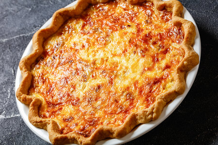 fluffy breakfast quiche with cheese and bacon in baking dish on dark concrete table, close-upの写真素材