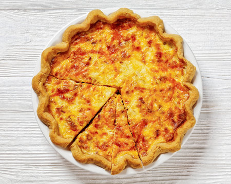 fluffy breakfast quiche with cheese and bacon filling on white plate on white wood table, horizontal view from above, flat lay, close-upの写真素材