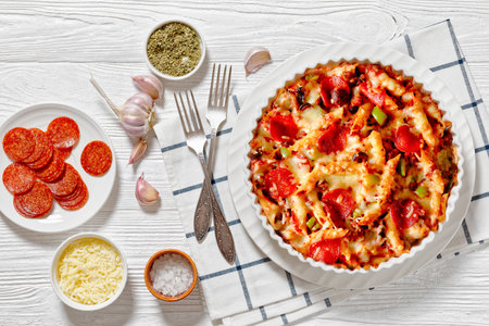 Pizza Casserole of tender penne pasta, browned beef meat, pepperoni, olives, bell peppers, and cheese smothered in marinara sauce in white baking dish on white wood table, flat layの写真素材
