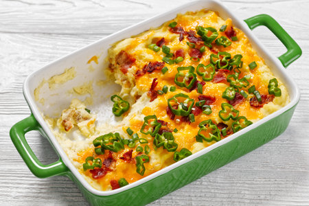 Loaded smashed potatoes with cheddar cheese, cream cheese, bacon, and cream in baking dishの写真素材