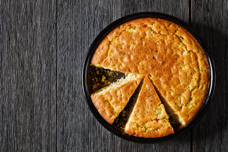Red pepper Cheddar Celery Cornbread cut on slices in baking dish on dark wooden table, horizontal...