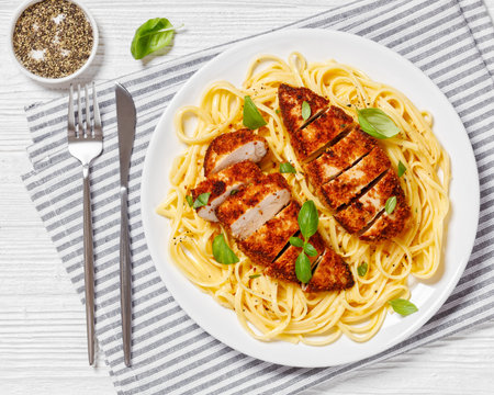 Chicken Scallopini of crusted chicken breast over lemon butter pasta on white plate on white wooden table, horizontal view from above, flat layの写真素材