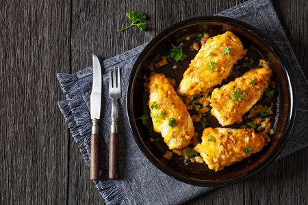 baked chicken breasts under cracker cheese crust in rustic baking dish on dark wooden table with cutlery, horizontal view from above, flat lay, free spaceの写真素材