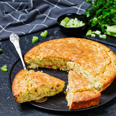 Red pepper Cheddar Celery Cornbread on black plate and a slice on cake shovel on concrete table with...