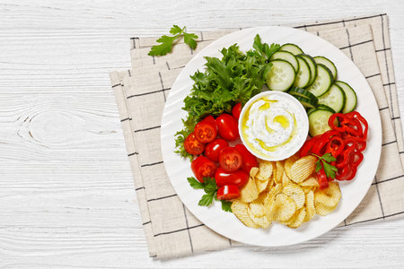 Potato Chips, leafy greens and vegetables snack platter with healthy yogurt ranch dip on a white wooden table, horizontal view from above, flat lay, free spaceの写真素材