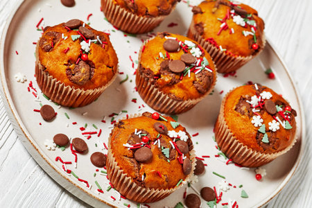 Christmas sweet potato muffins topped with holiday sprinkles and chocolate drops on plate on white wooden table, close-upの写真素材
