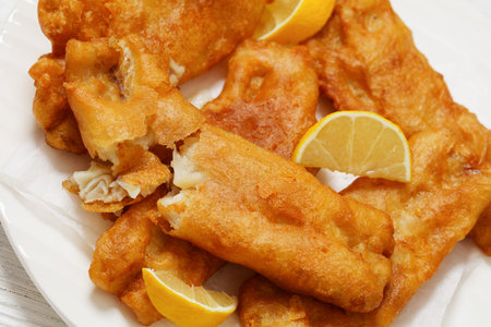 deep fried crispy beer batter fish fillet on white plate with lemon slices, Dutch angle view,...