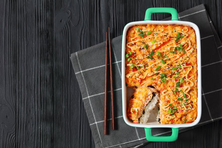 sushi bake, baked deconstructed salmon sushi rolls in baking dish on black wooden table with chopsticks, horizontal view from above, flat lay, free spaceの写真素材