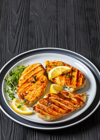 boneless skinless juicy grilled chicken cutlets with thyme and lemon slices on plate on black wooden table, vertical view, close-up, free spaceの写真素材