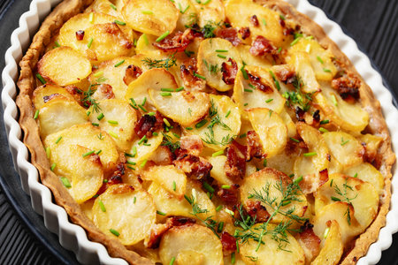 Irish potato pie of crispy crust layered with potatoes, bacon, dill and onion in baking dish on black wooden table, Dutch angle view, close-upの写真素材