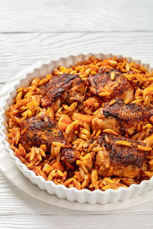 One pan baked Greek chicken orzo stew in tomato based sauce, giouvetsi youvetsi in baking dish on white wooden table, vertical view from above, close-up, free spaceの写真素材