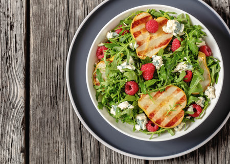 grilled pear salad with blue cheese, arugula and fresh ripe raspberries in white bowl on rustic wooden table, horizontal view, flat lay, close-up, free spaceの写真素材