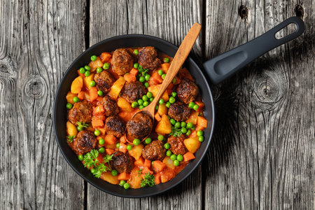 Turkish meatball stew, sulu kofte, hearty dish with potatoes, carrot and green peas simmered in tomato sauce served on a pan on rustic gray wooden table, flat lay, close-up, free spaceの写真素材