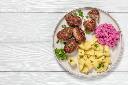 frikadeller, danish meatballs of minced pork with boiled potatoes and beetroot salad on plate on white wooden table, horizontal view from above, flat lay, free spaceの写真素材