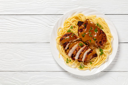 Chicken Lazone poured with seasoned creamy sauce served over pasta noodle on white plate on white wooden table, horizontal view from above, flat lay, free spaceの写真素材