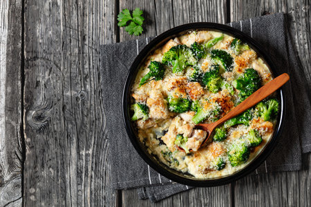 Chicken Divan, bite size of chicken meat smothered in creamy sauce with broccoli topped with panko in baking dish on rustic wooden table with spoon, horizontal view from above, flat lay, free spaceの写真素材