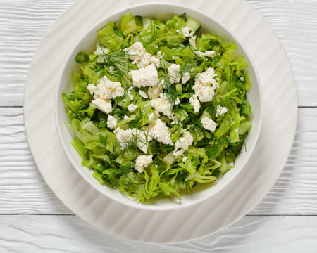 Classic Greek lettuce salad sprinkled with crumbled feta cheese, Maroulosalata, in a white bowl on white wooden table, horizontal view from above, flat lay, close-upの写真素材