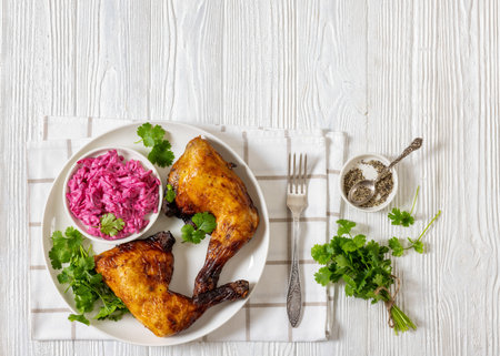 roast crispy and juicy chicken leg quarters with beetroot mayo salad and fresh coriander on a plate on white wooden table with fork, horizontal view from above, free spaceの写真素材